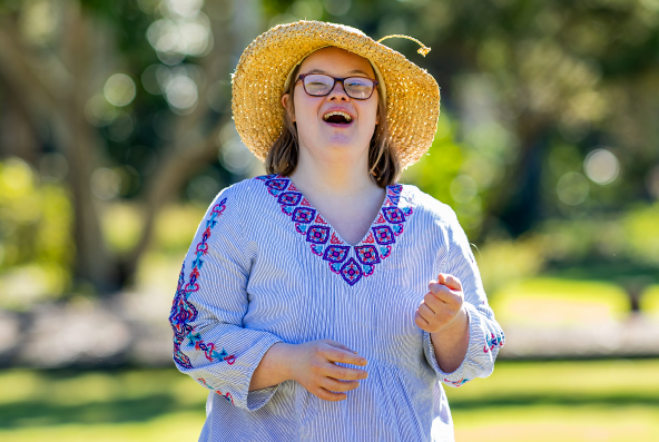 A girl with a straw hat is smiling outside in a park