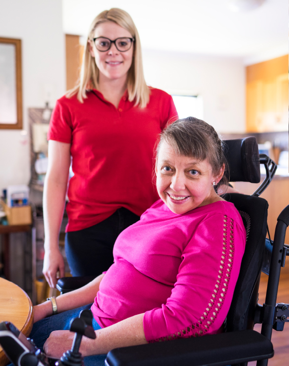 A woman in a wheelchair sits in her home with a support worker behind her