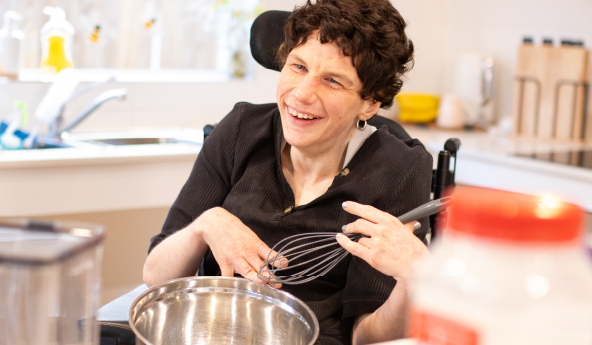 A person sits in a wheelchair in their home, mixing with a mixing bowl