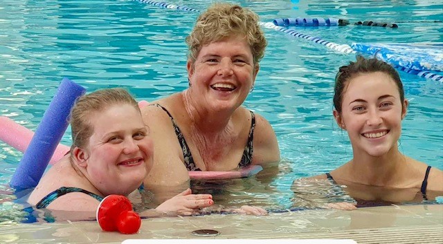 Three people swimming and smiling at the camera